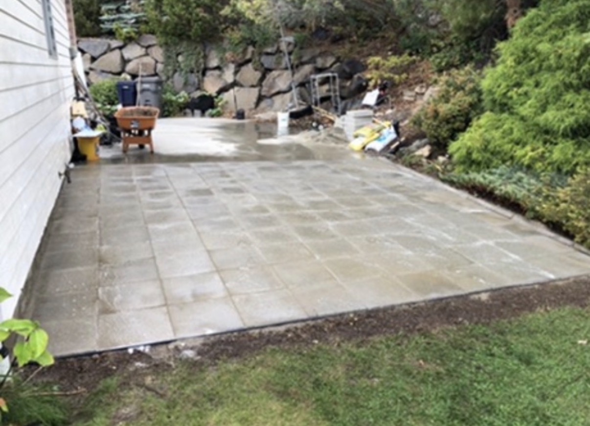 New paver patio installed beside a home below a rock wall